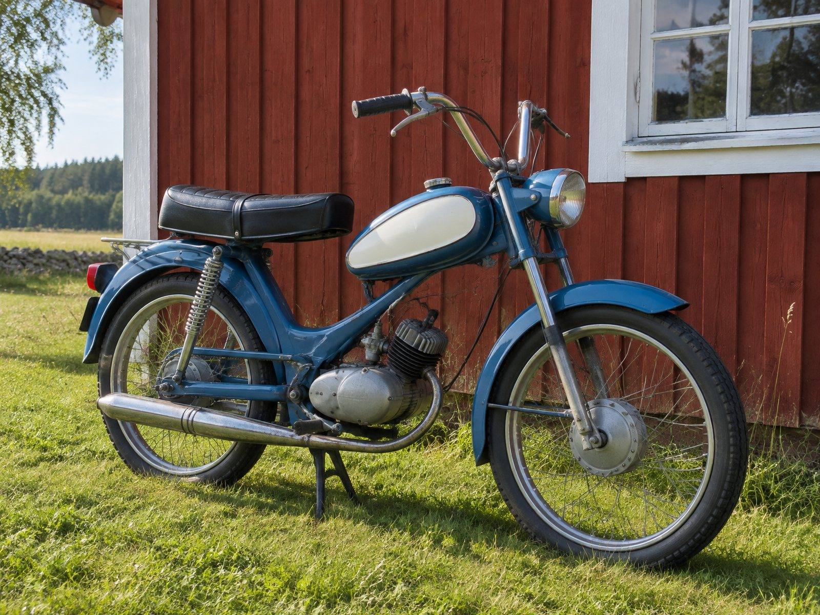 En blå veteranmoped parkerad på gräset framför en röd ladugårdsvägg